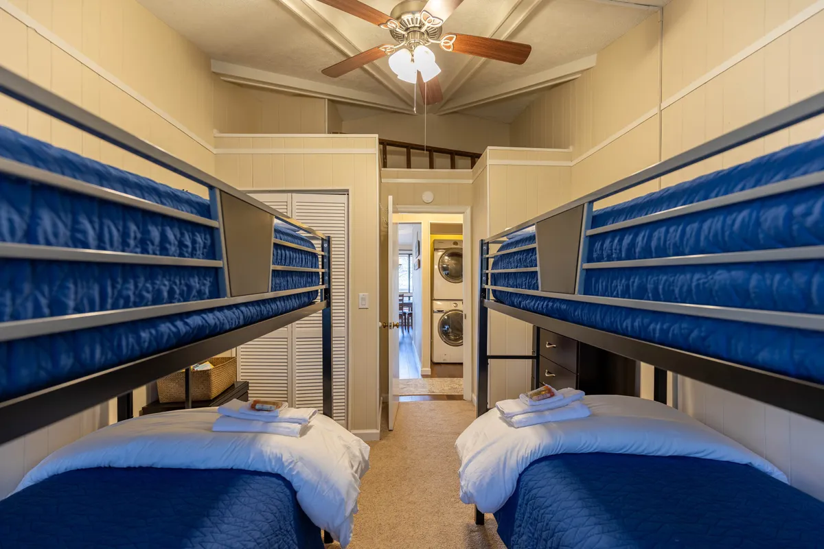 Inside, the image features bunk beds, a visible ceiling fan, and a laundry area. The ceiling fan sits centrally above, providing airflow, while the beds and laundry suggest convenience and comfort for families or groups.