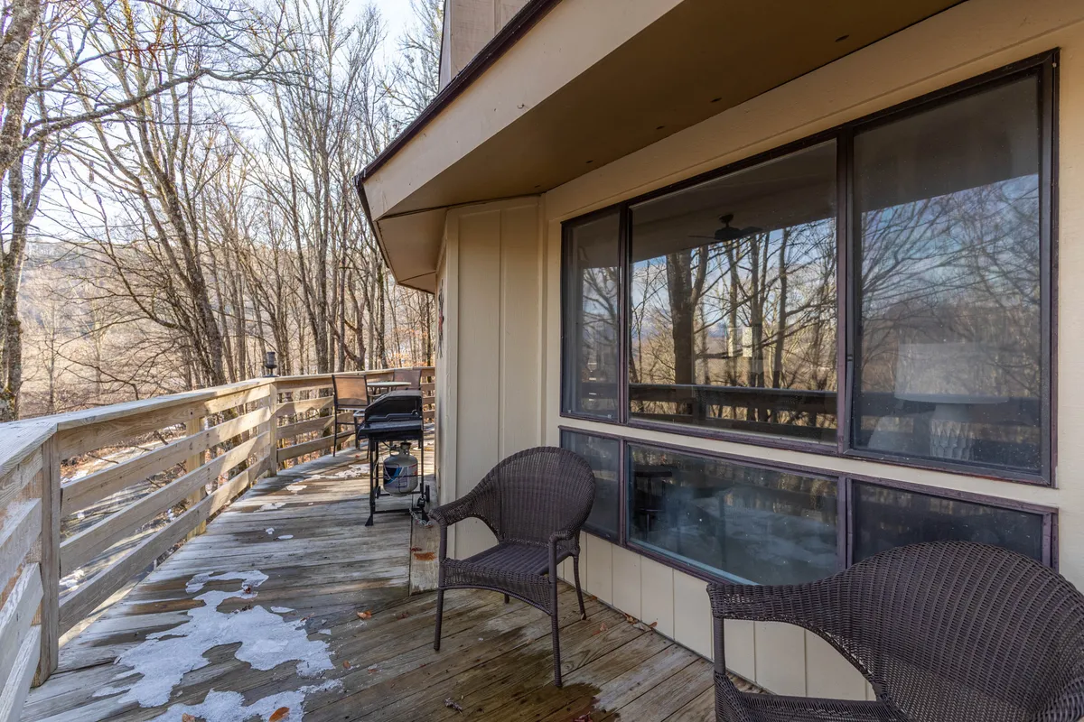 The scene shows a deck with comfortable chairs and a grill, surrounded by trees. The space is designed for outdoor dining, morning coffee, or simply enjoying the mountain views, making it perfect for unwinding after a day of adventure.