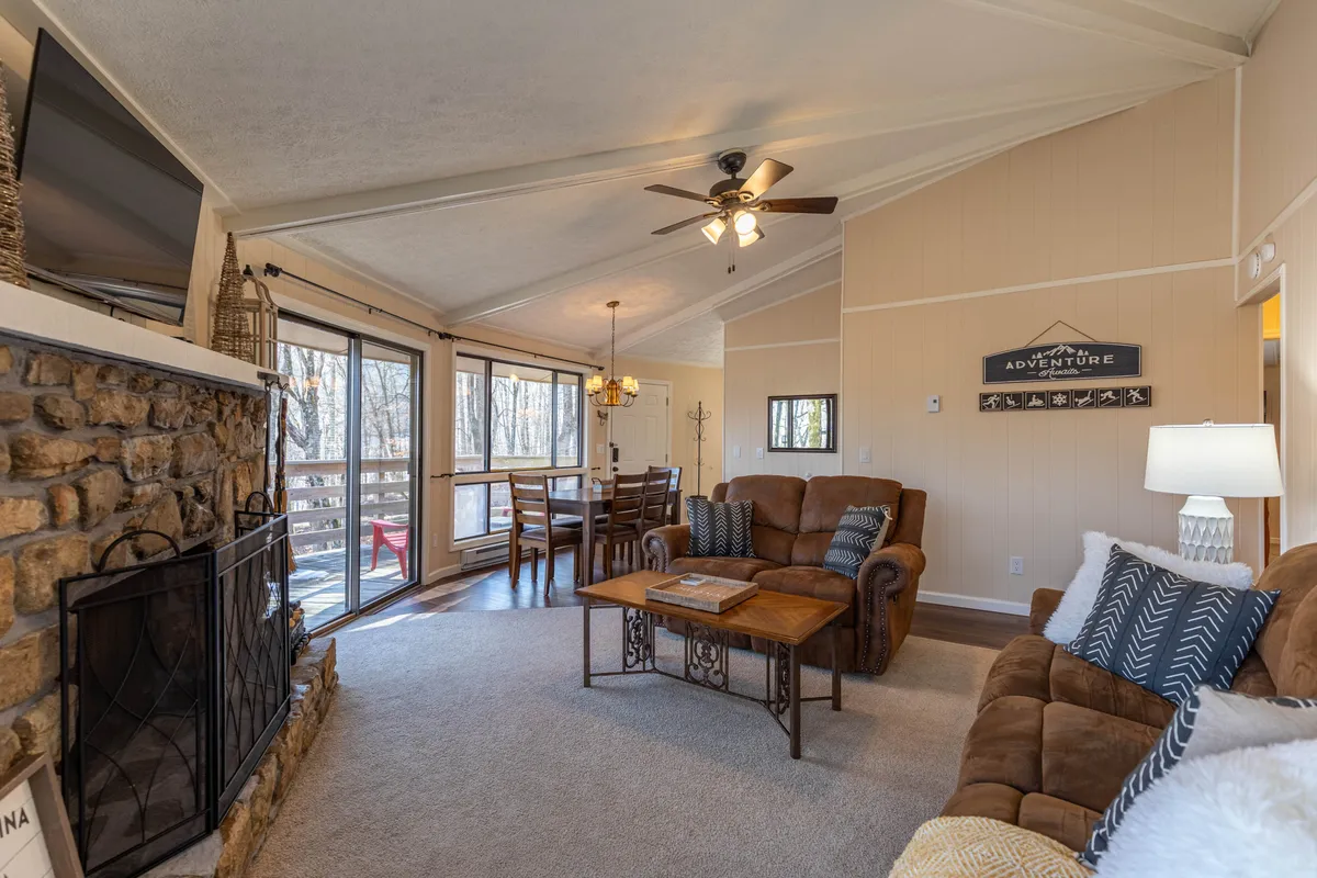 This image showcases a spacious, warmly lit family room anchored by a striking stone fireplace. Comfortable seating surrounds a wooden dining table, and large windows allow natural light to flood the space. The room's round architecture and inviting furnishings create a central gathering area ideal for family and friends.